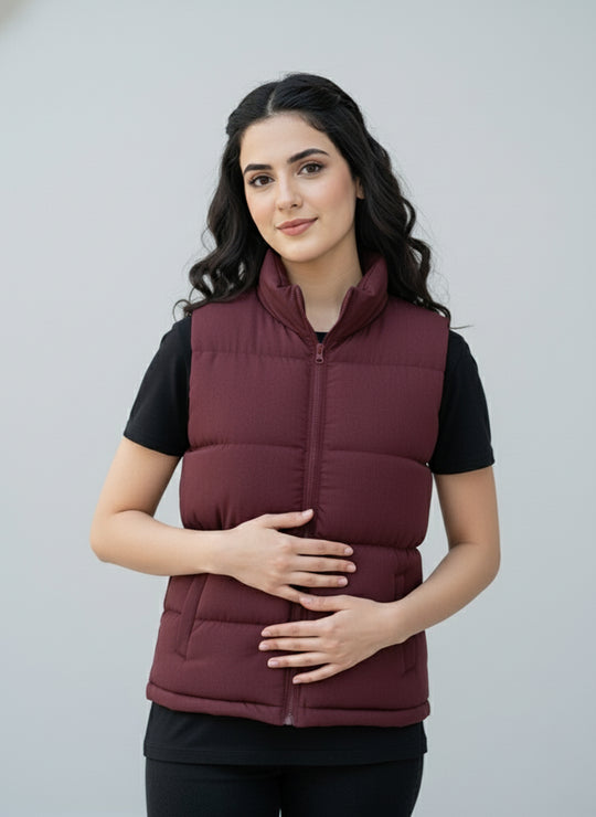 Woman wearing a maroon puffer vest over a black shirt against a gray background