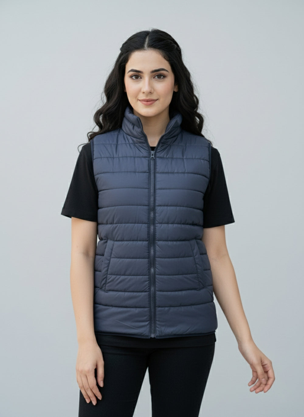 Woman wearing a blue puffer vest over a black shirt on a gray background