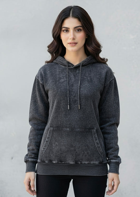 Woman wearing a acid washed hoodie against a plain background