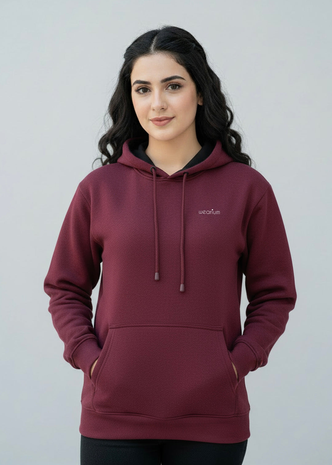 Woman wearing a maroon hoodie with a brand logo on a plain background