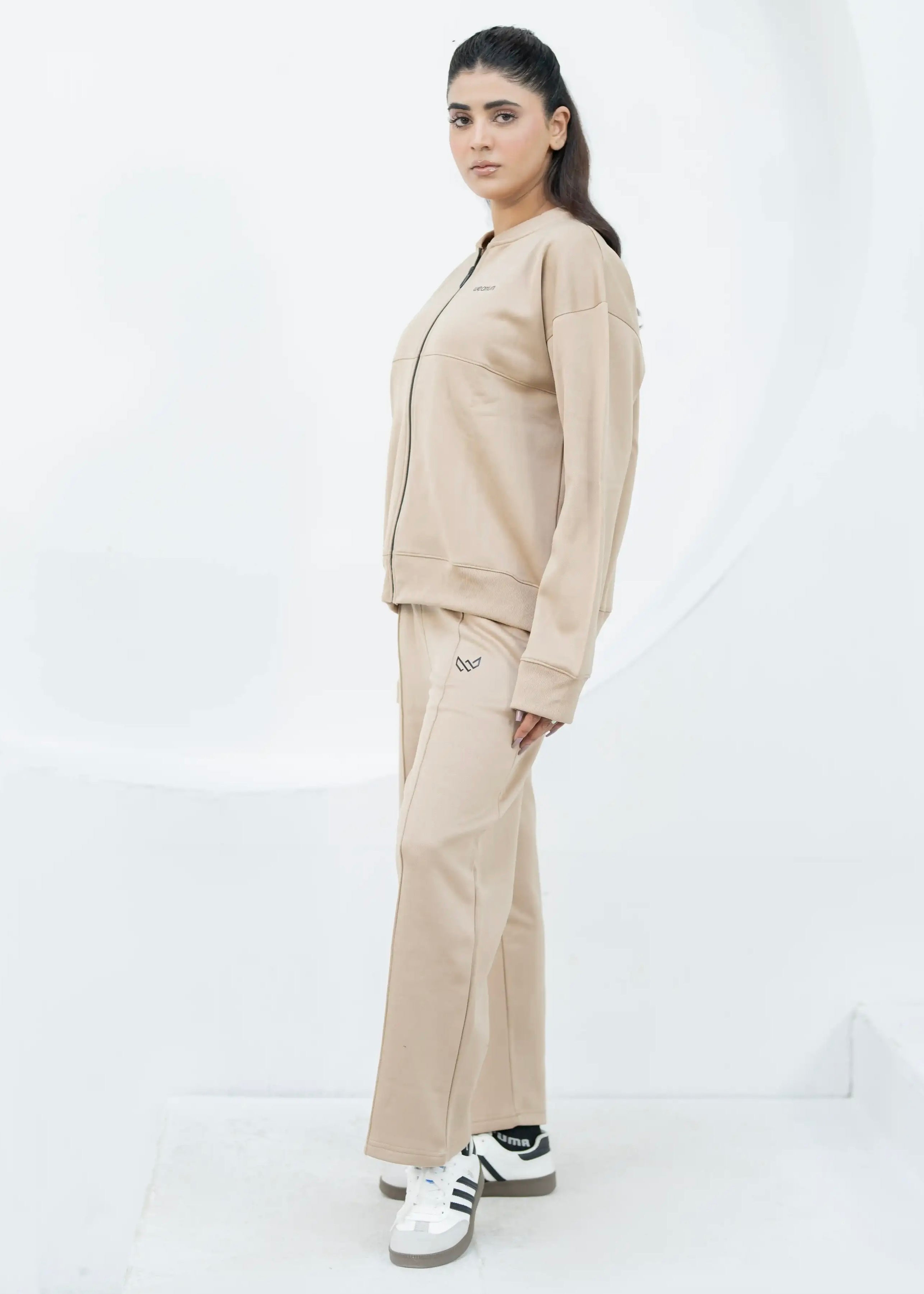 Person wearing a beige tracksuit with Adidas shoes on a white background