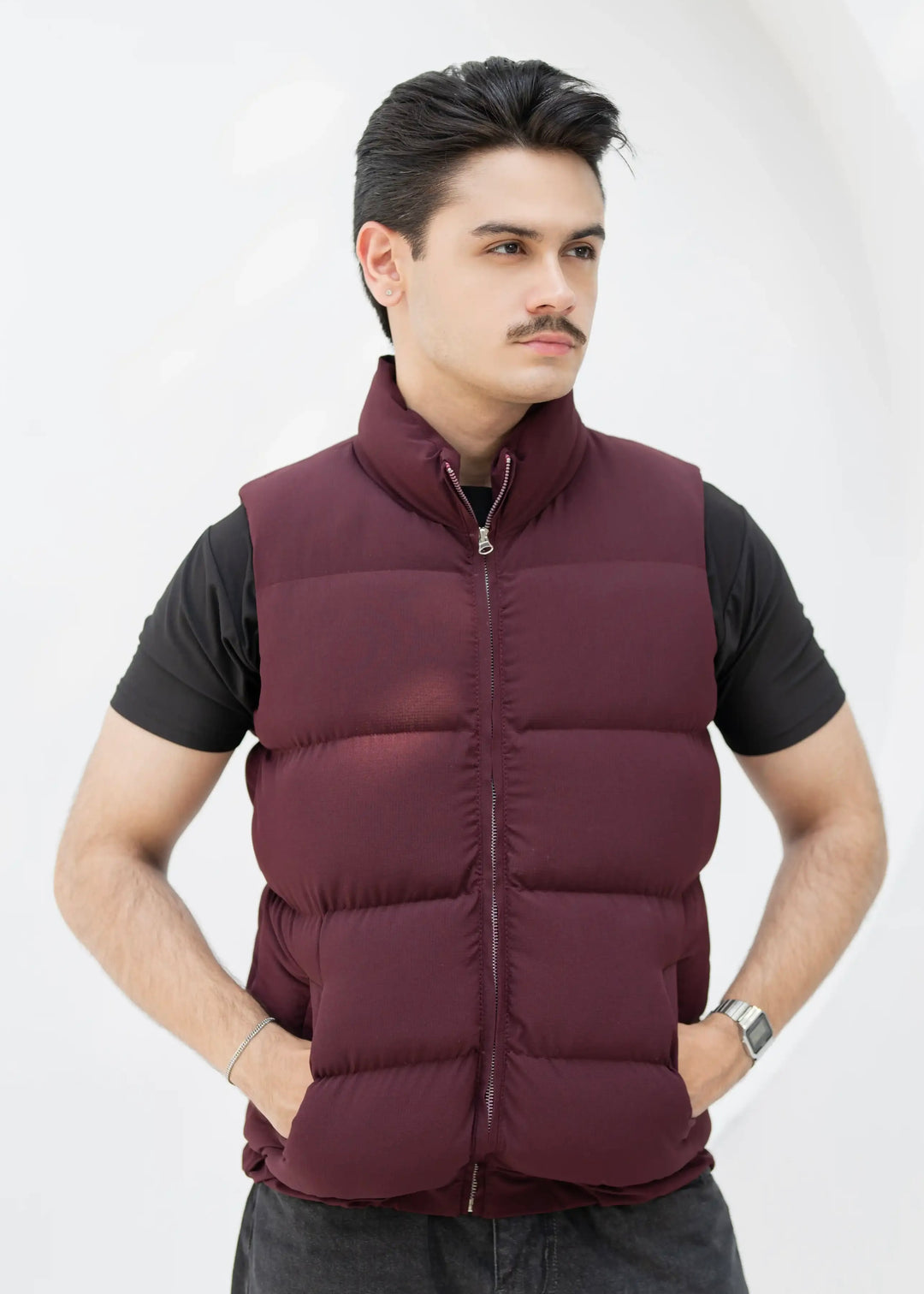 Man wearing a maroon puffer vest over a black shirt on a white background