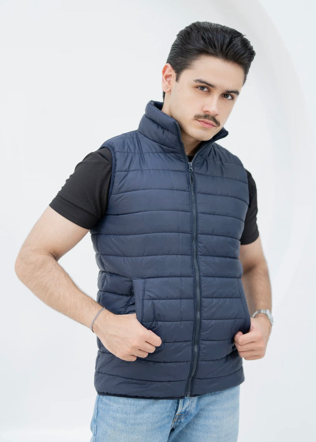 Man wearing a blue puffer vest over a black shirt on a white background