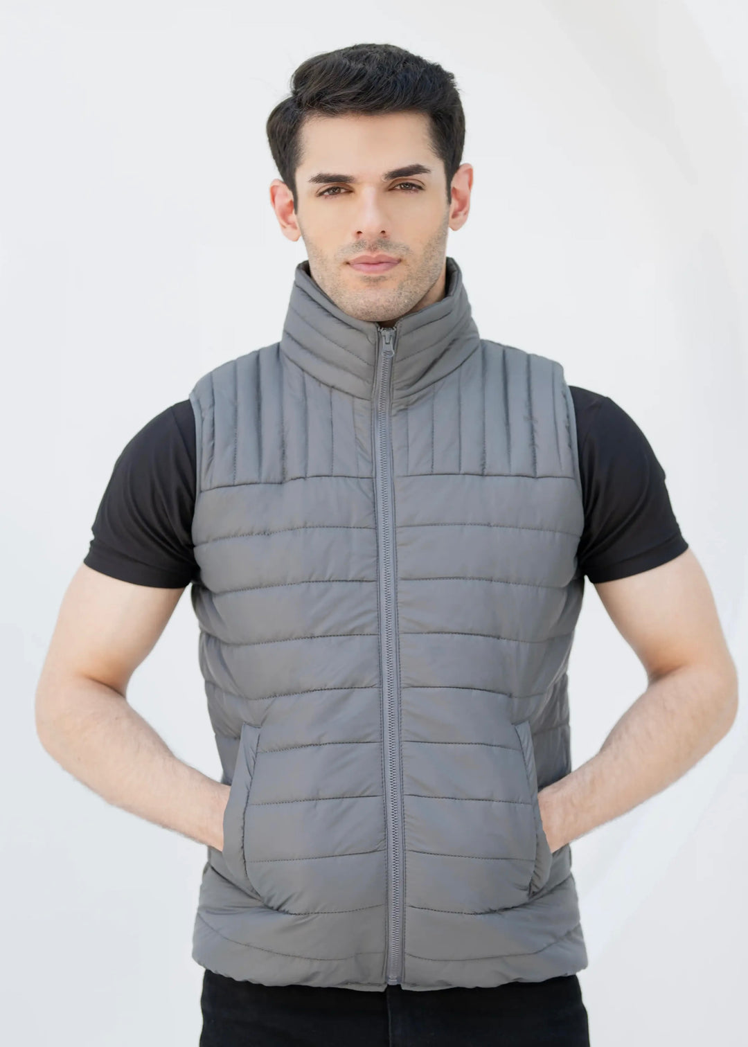 Man wearing a gray puffer vest over a black shirt on a white background