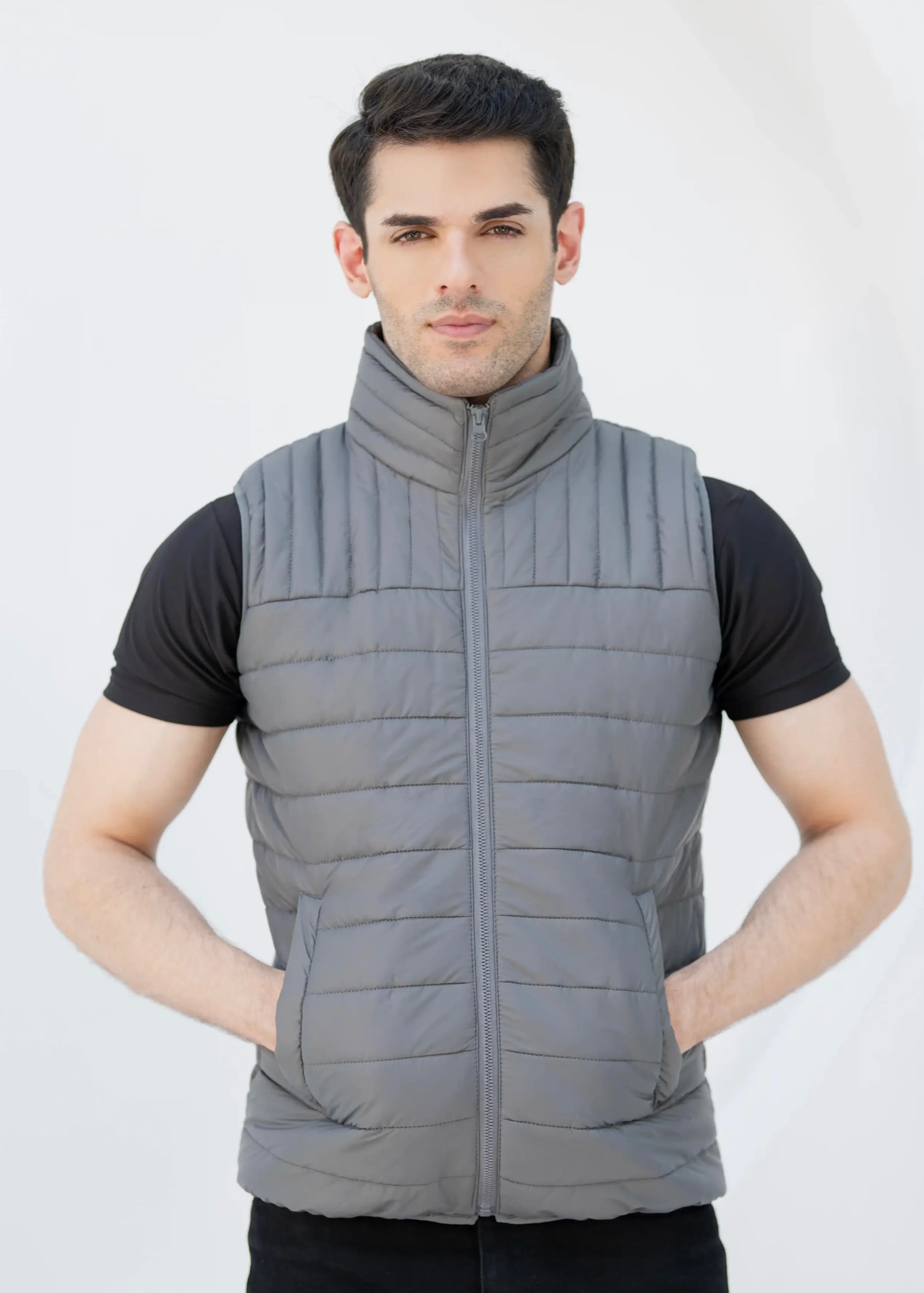 Man wearing a gray puffer vest over a black shirt on a white background